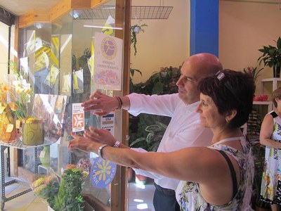Foto 2. L'alcalde accidental i una comerciant enganxen el distintiu a l'entrada de la botiga.