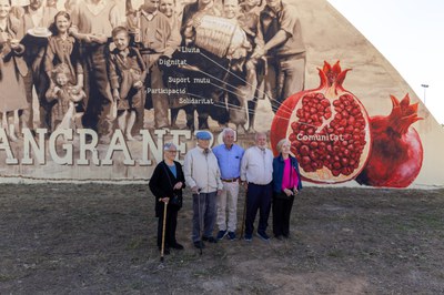 Veïns i veïnes davant el mural de Roc Blackblock, on surten representats.