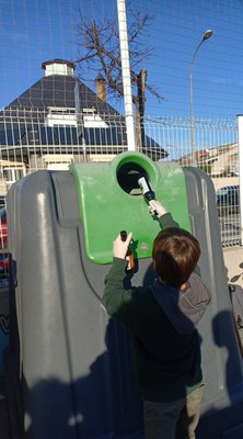Un nen diposita ampolles en un contenidor verd
