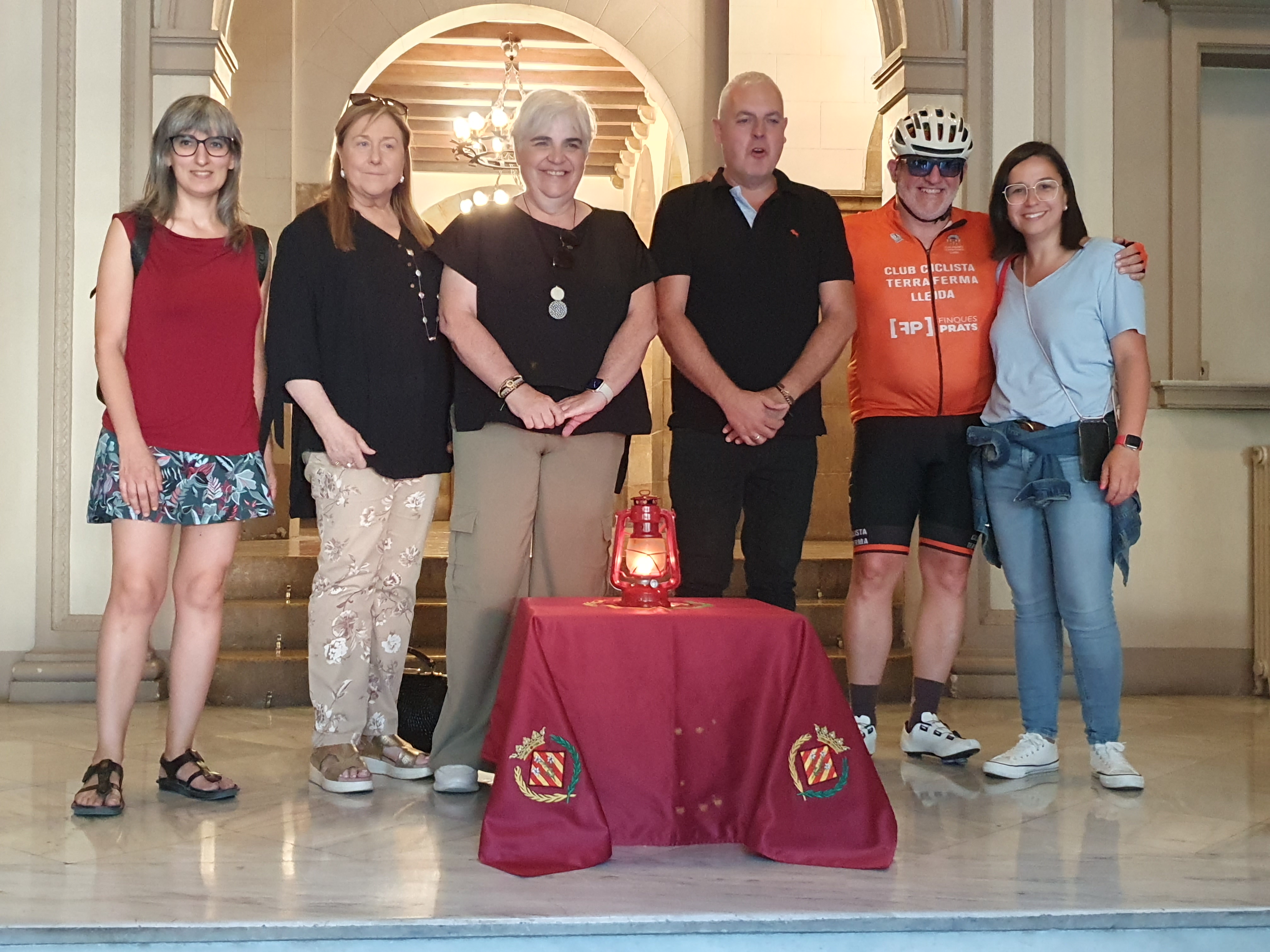 La tinent d'alcalde, Carme Valls, les regidores Jordina Freixanet, Sandra Castro i Rosa Jové, el president de l'Associació Flama del Canigó de Lleida, Enric Figueres, i un membre de l'equip ciclista que ha portat la Flama, a l'entrada de la Paeria