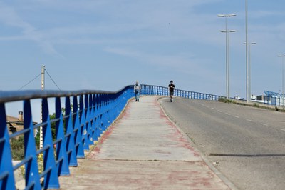 Un vianant i el conductor d'un patinet creuen el pont.